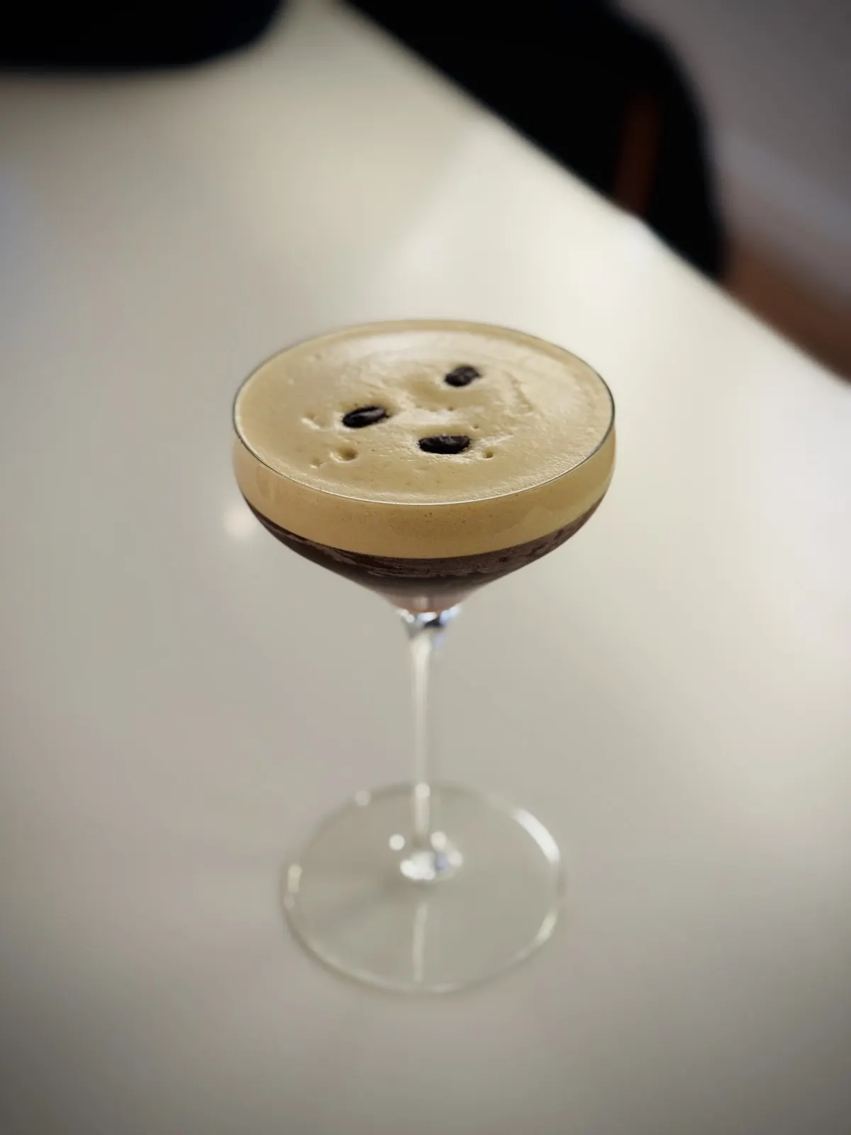 一杯 Espresso Martini，表面有咖啡色泡沫并装饰咖啡豆