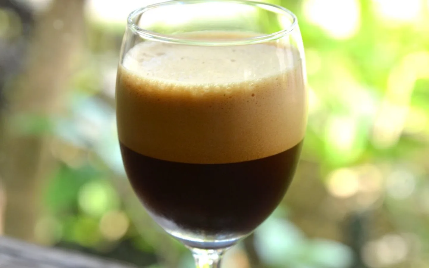 一杯盛在高脚杯中的意式冰摇咖啡 Shakerato，深色咖啡上覆盖厚实浅棕泡沫