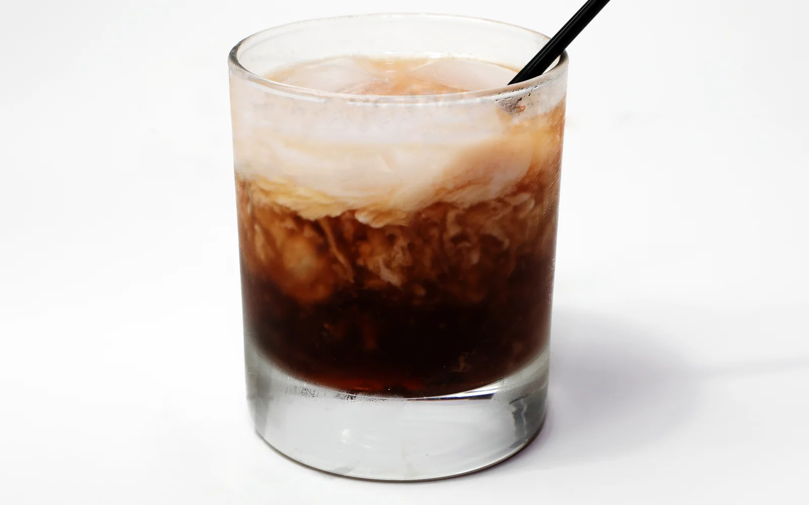装有大冰块的短杯白俄罗斯鸡尾酒，咖啡色酒液上方有浅色奶油旋纹